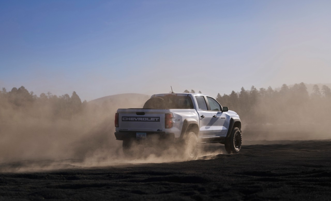 Rear view of Silver Chevrolet Colorado driving through dust. 