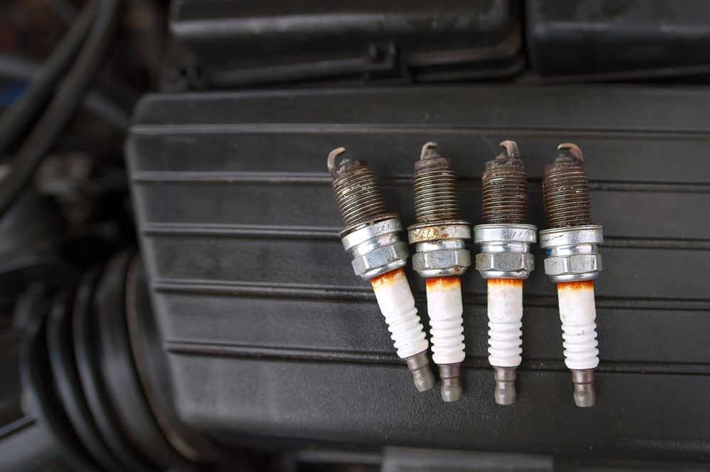 Four spark plugs lined up in a row next to each other, the color of the spark plugs is white and theyre set against a black background of some sort