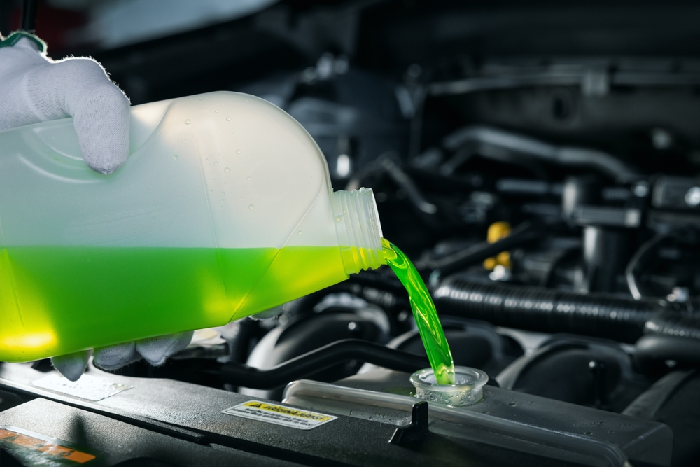 close up shot of a mechanic pours green coolant a vehicle's coolant reservoir