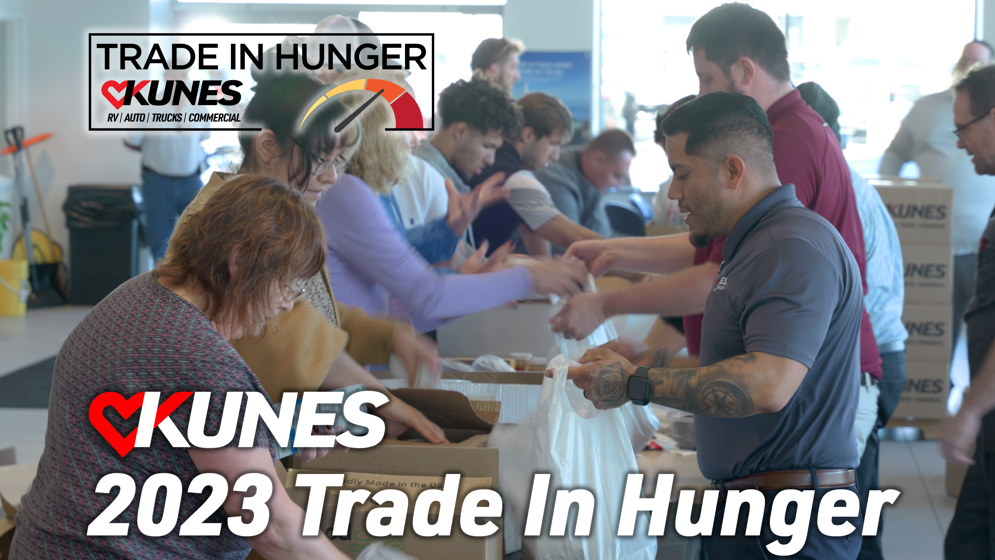 text over image of Kunes employees packing food boxes; text reads: TRADE IN HUNGER KUNES RV | AUTO | TRUCKS | COMMERCIAL; KUNES 2023 Trade In Hunger