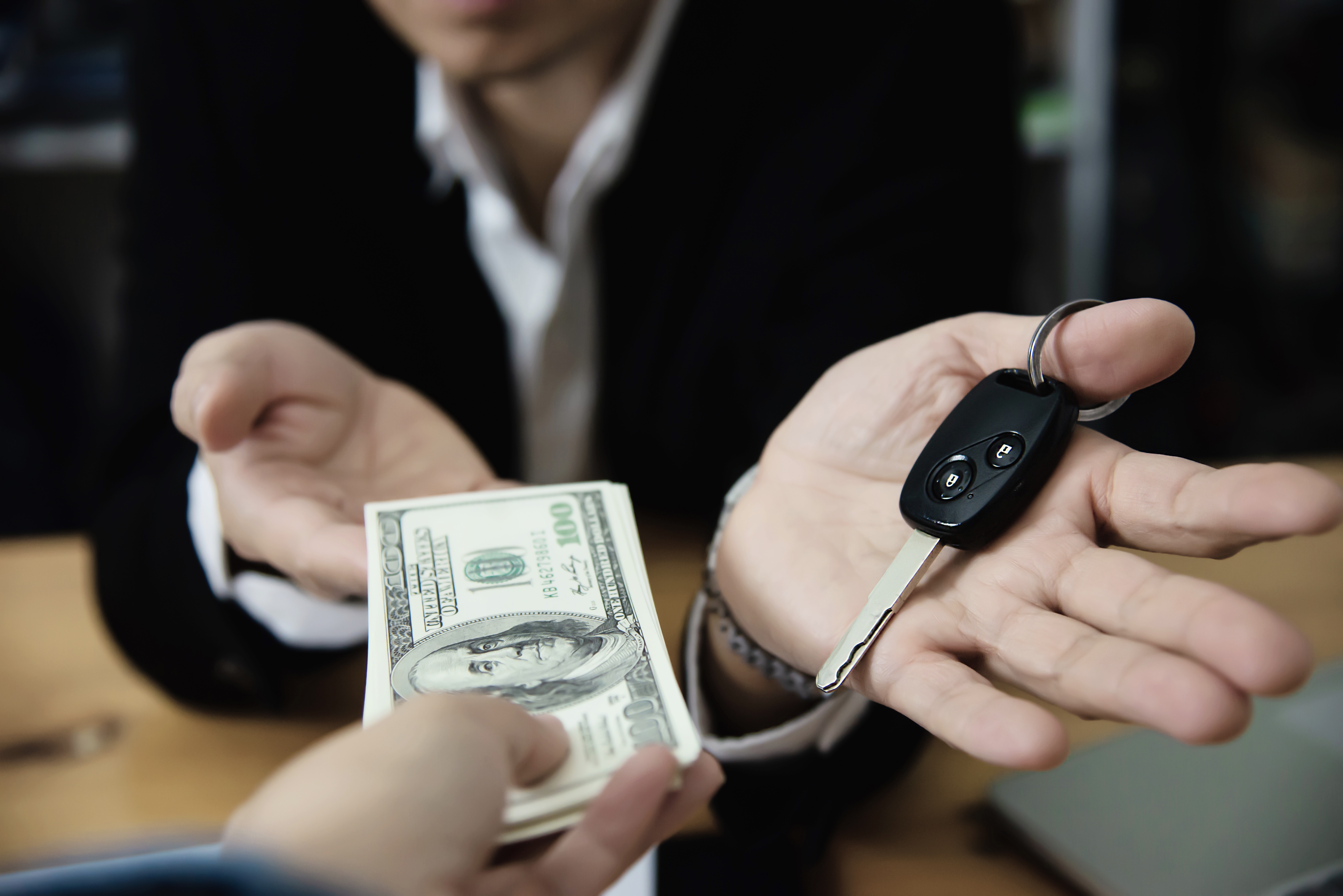 A person handing over their car keys to trade in for money
