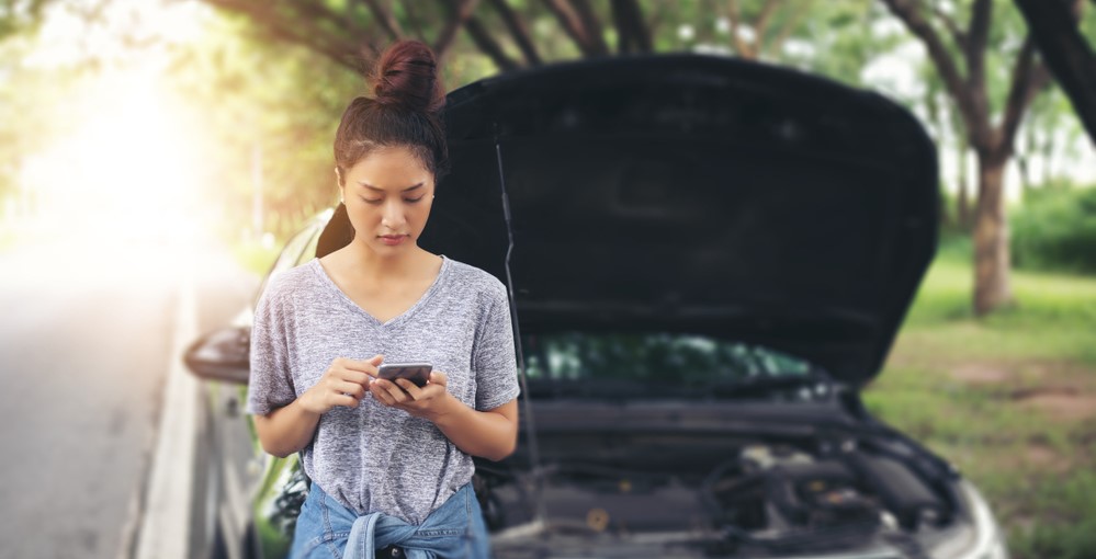 girl looking as cell phone to call for assistance with her broken down car