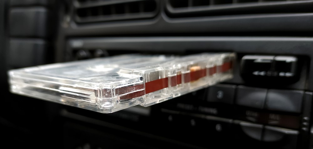 cassette tape sits half-way inserted into a cassette player inside of a vehicle; close-up shot