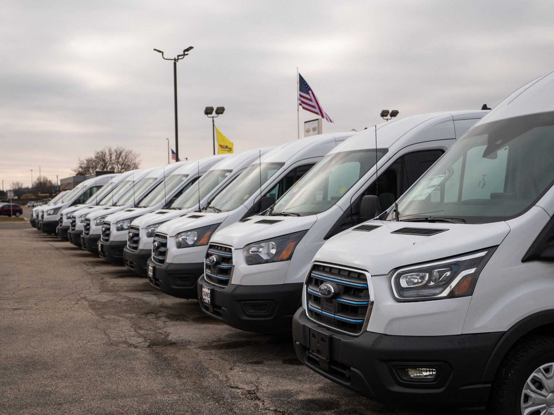 a parked row of white Ford transit vans in Kunes dealership lot