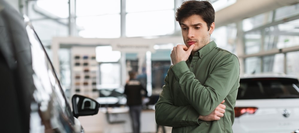 man thinks about buying car at the dealership
