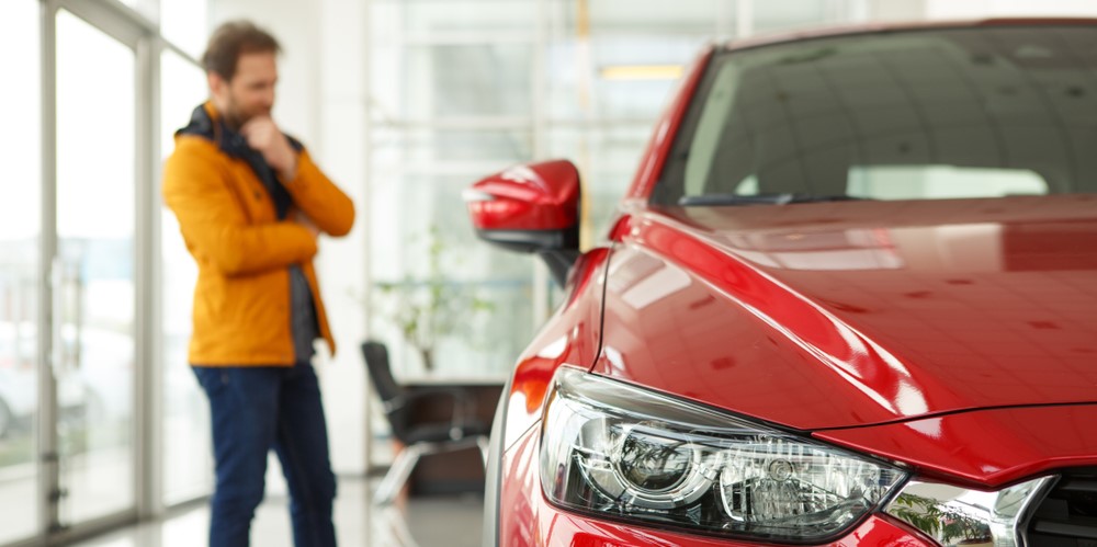 out of focus: man thinking, while looking at a red car; in focus: red car