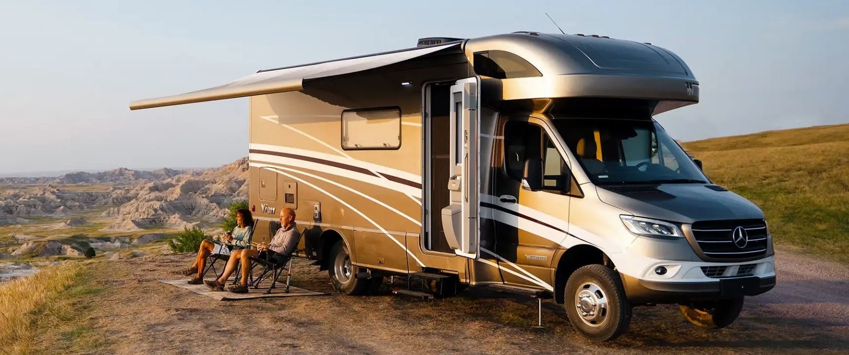 older couple sitting in lawn chairs outside of their Winnebago RV as they watch the sunset from an overlook point