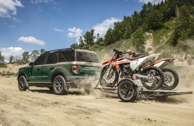 Green 2024 Ford Bronco Sport Towing a Dirt Bike Trailer on Dirt Road