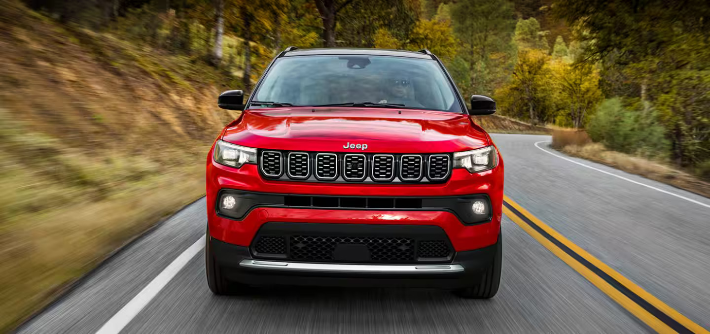 A red Jeep Compass driving on a road.