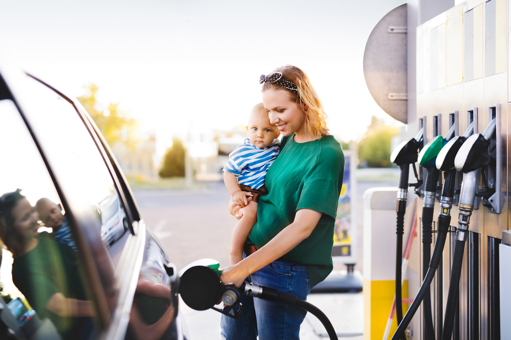 mother holds her baby as she safely pumps gas at a gas pump