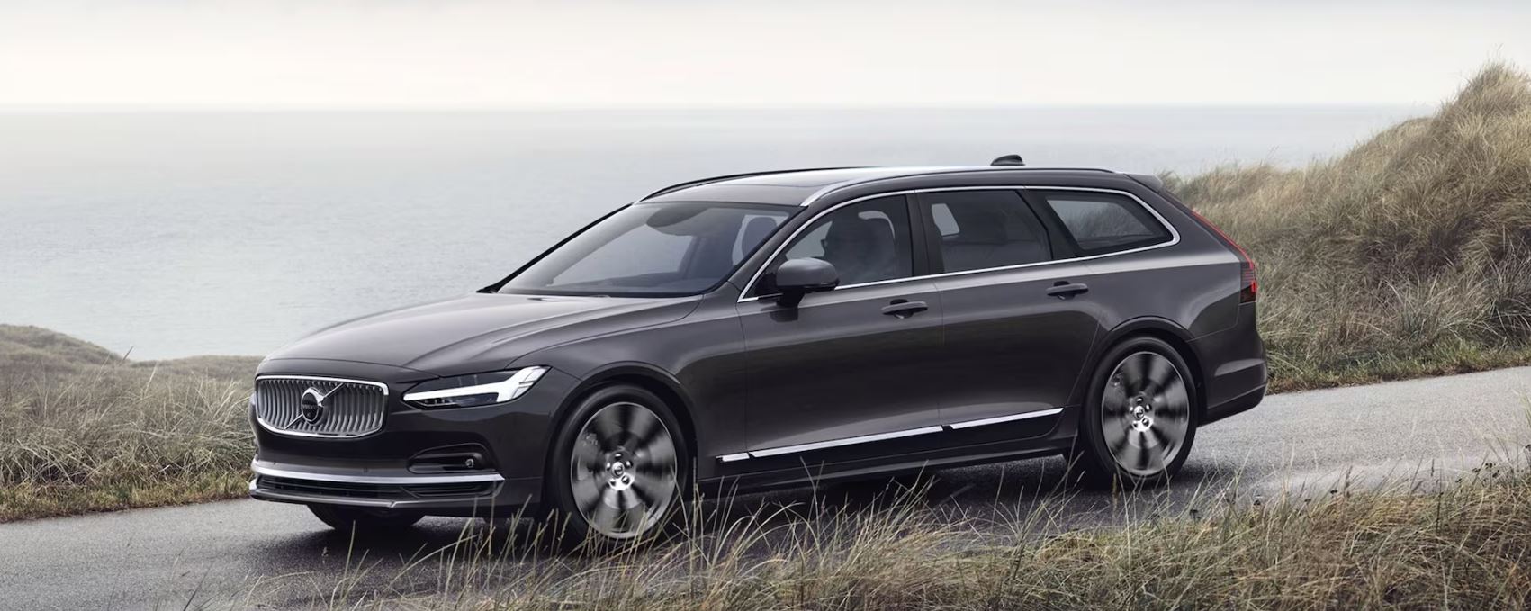 black 2023 Volvo V90 Cross Country driving on a road along the shoreline