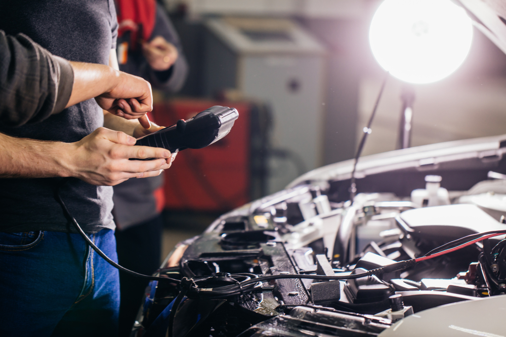 technicians holding diagnostic tool hooked up to car battery