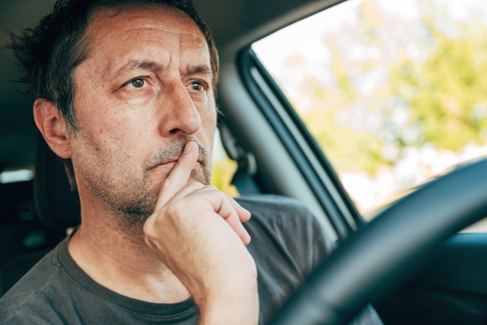 man thinking while sitting in driver's seat of vehicle