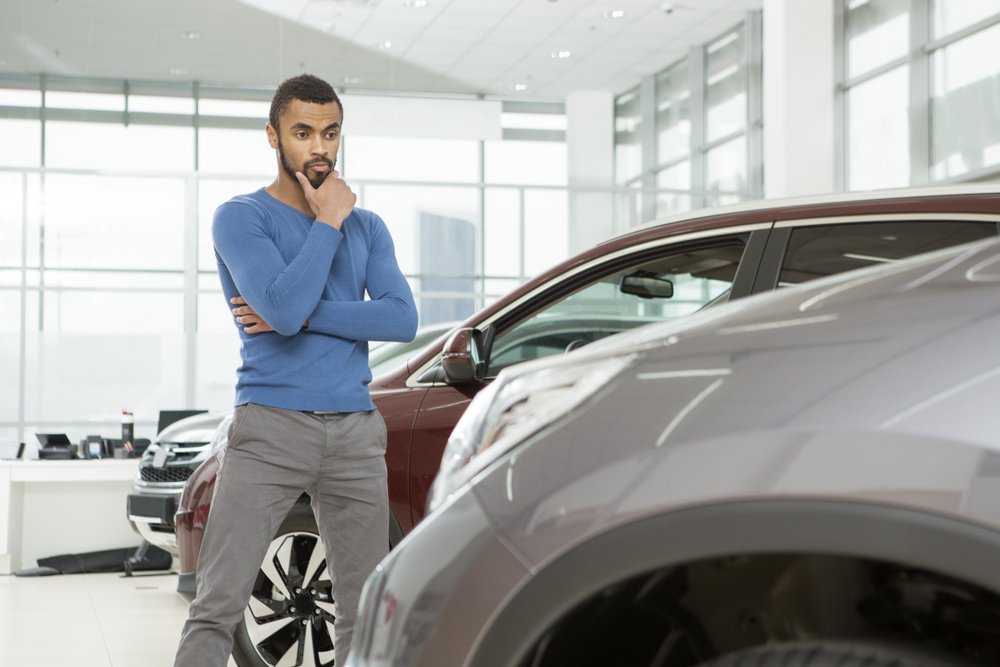 man deep in thought while staring at a car in a dealership