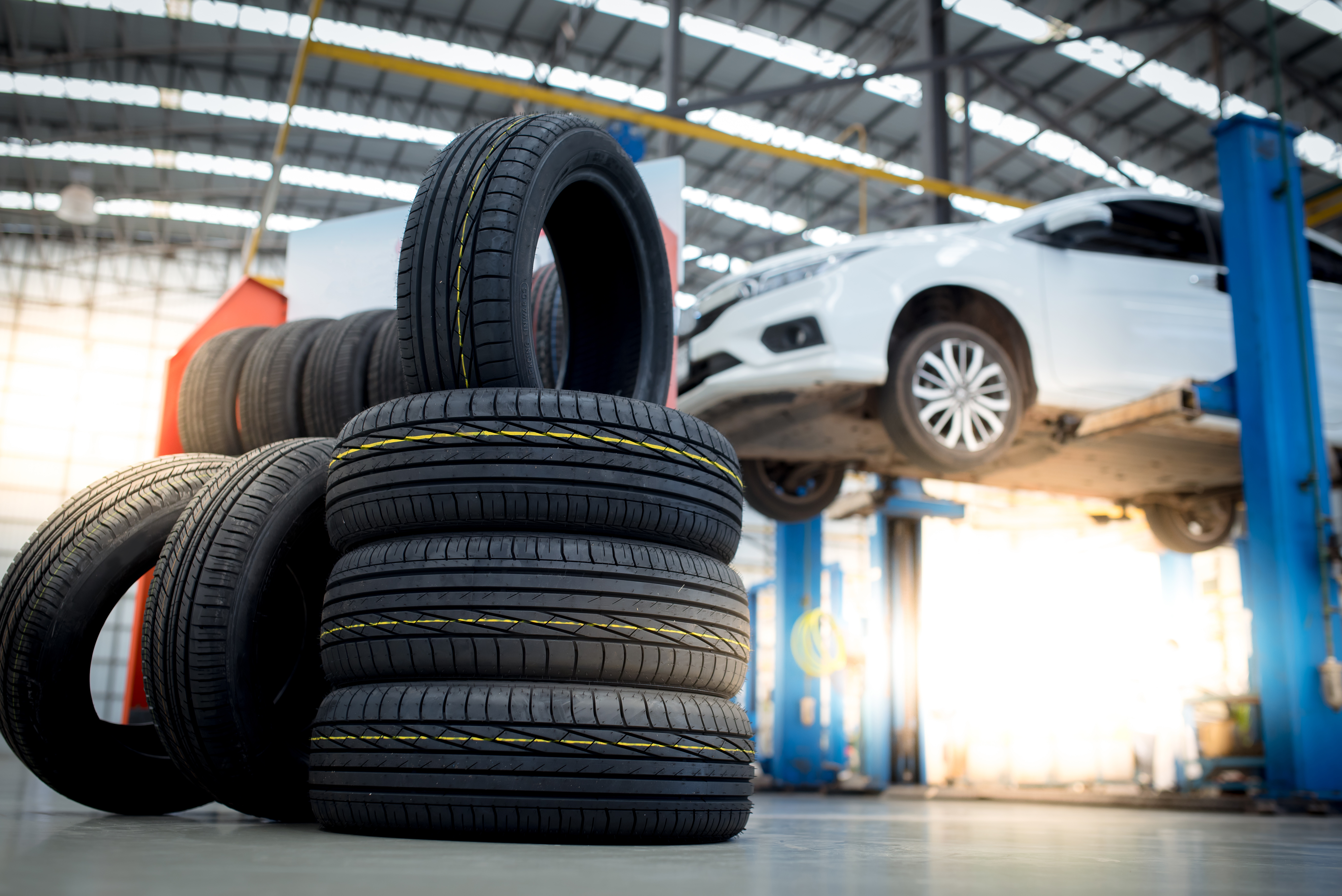 stack of tires pictured in front of a white car on a mechanic lif