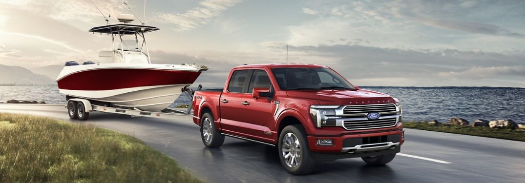 Red 2024 Ford F-150 Towing a Boat on a Coast Road