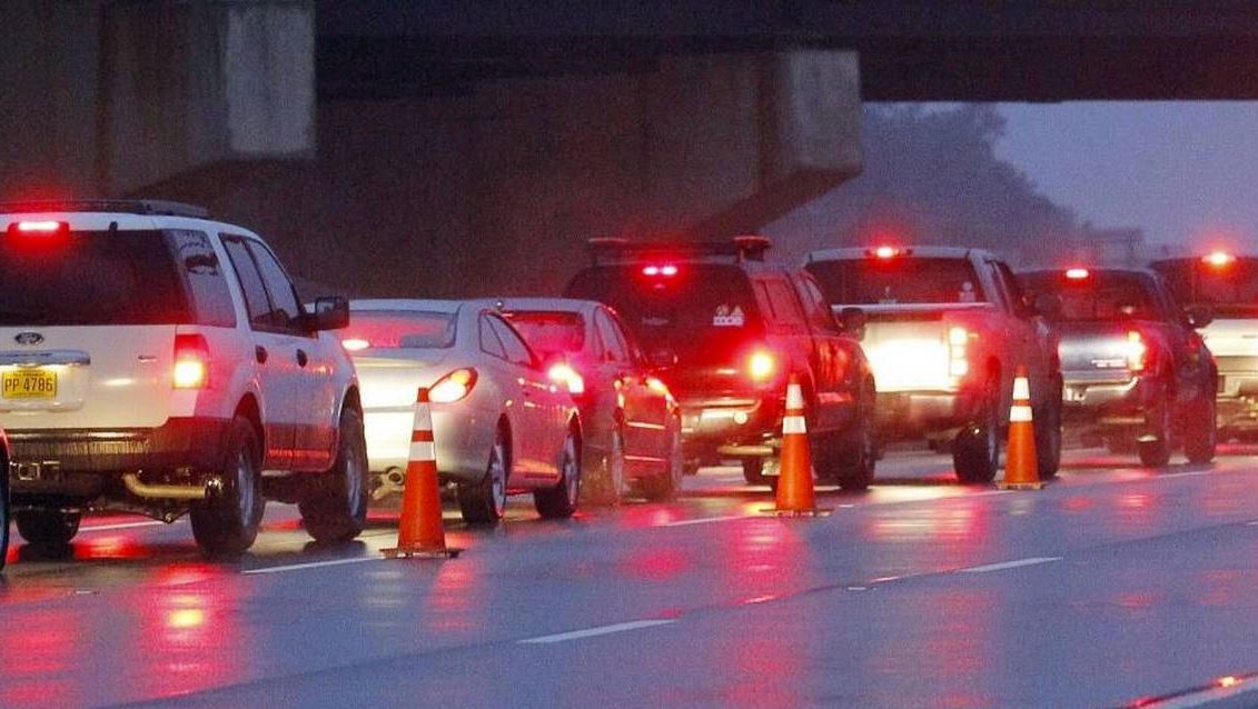 line of vehicles with their brake lights on in a construction zone lined with orange cones