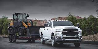 A white 2021 Ram 2500 towing a yellow construction digger through a southwest american mountain scene