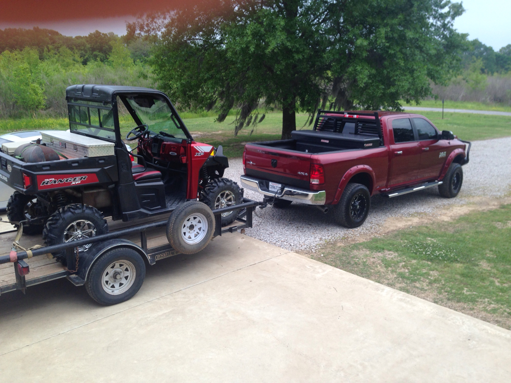A candy apple red Ram 2500 pulling a Red Polaris RANGER on a trailer in a wooded area.