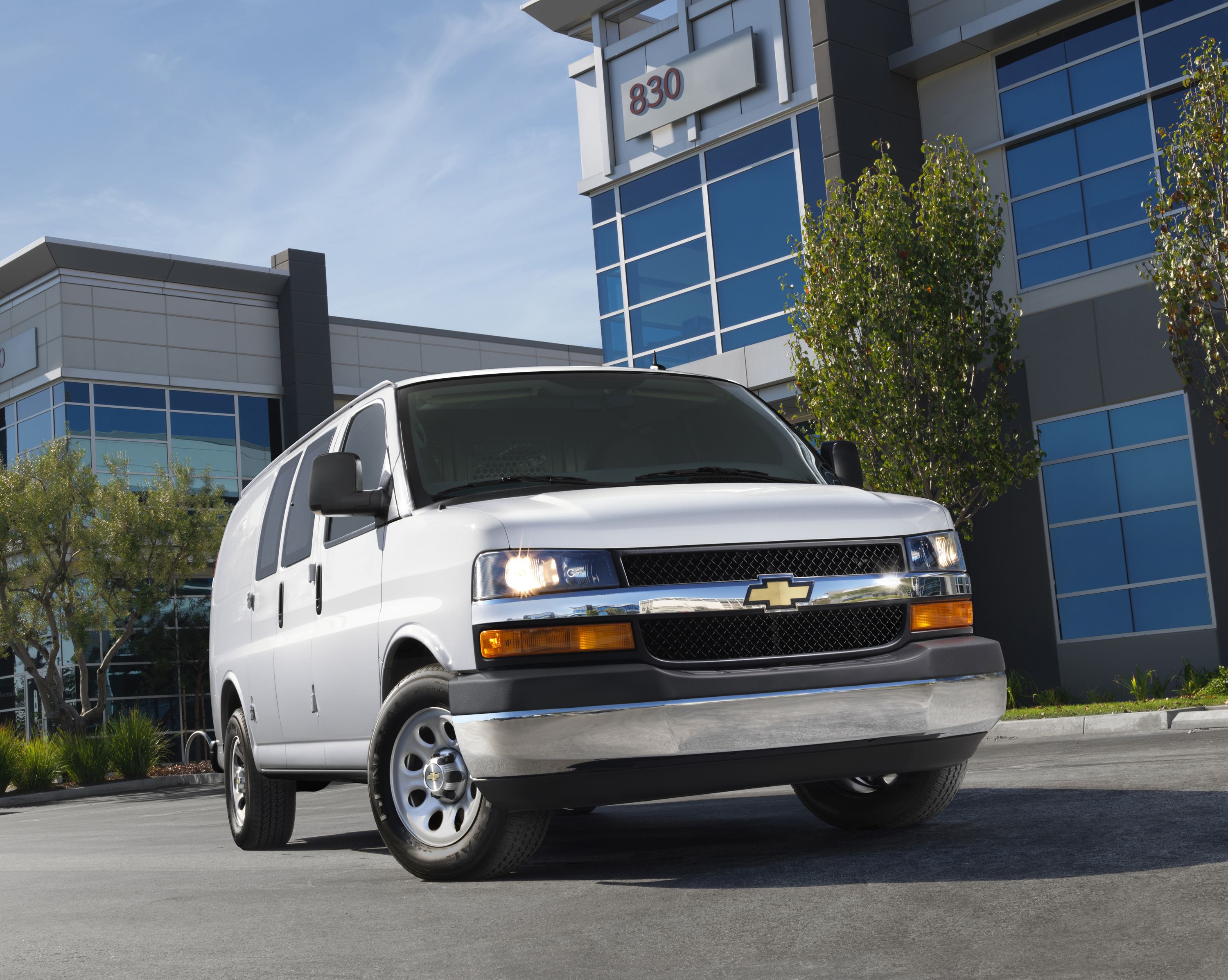 3/4 view of white Chevrolet Express in front of office buildings. 