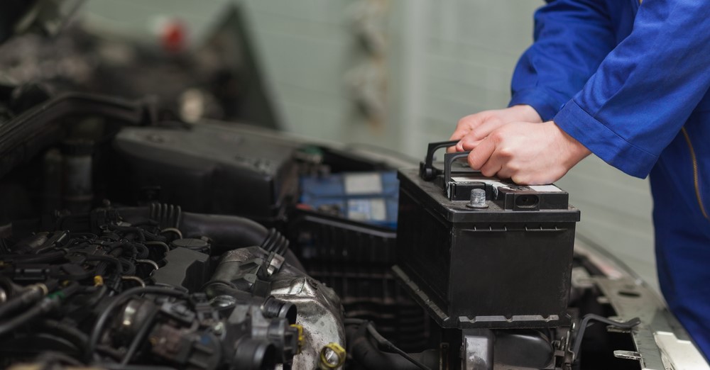mechanic about to instal car battery into vehicle; only shows their hands