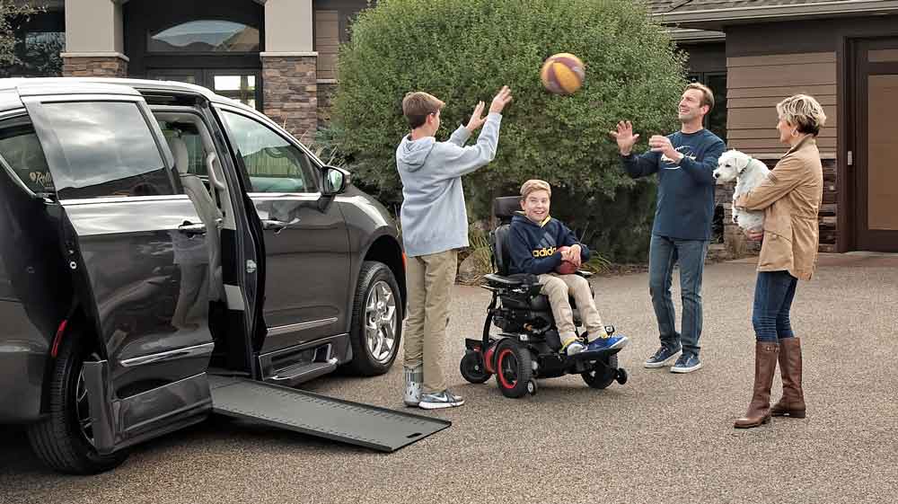 family plays monkey in the middle with son in power chair, while mom holding their dog watches.