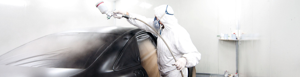 Auto repair technician, dressed in safety gear, painting a car in a spray booth.