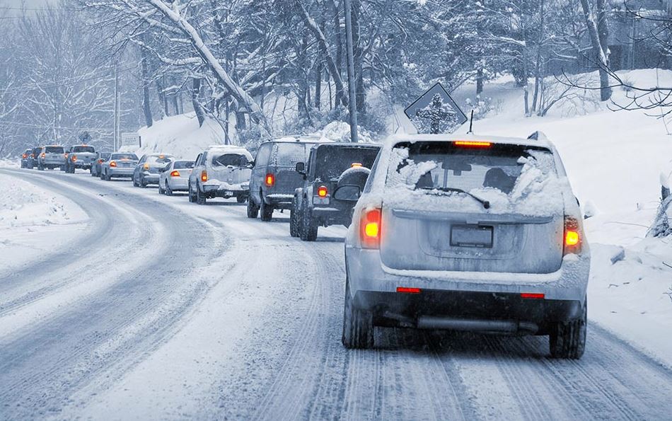 line of vehicles driving down a snowy road in winter