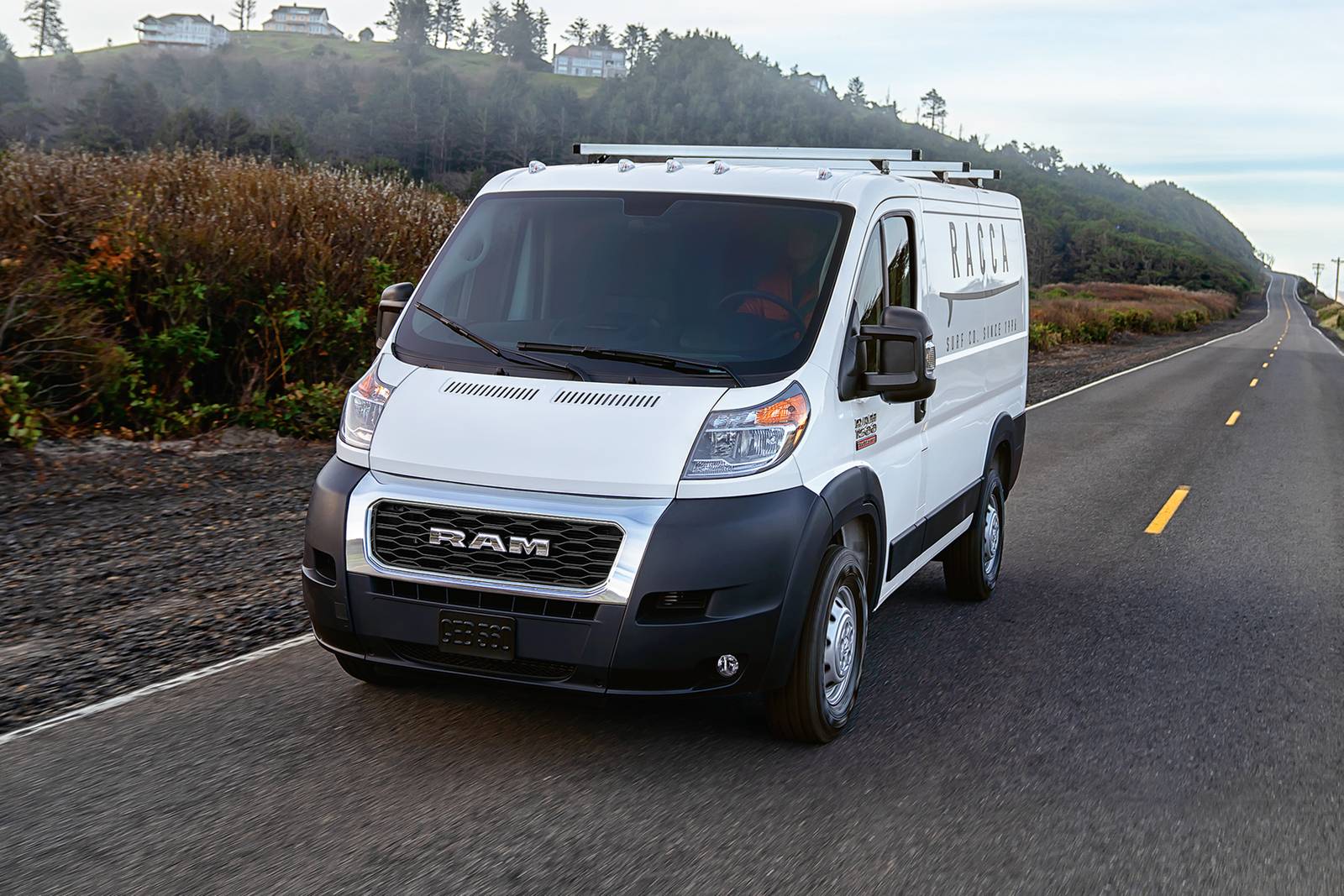 a white ram promaster 1500 driving down a suburban street in a front view.