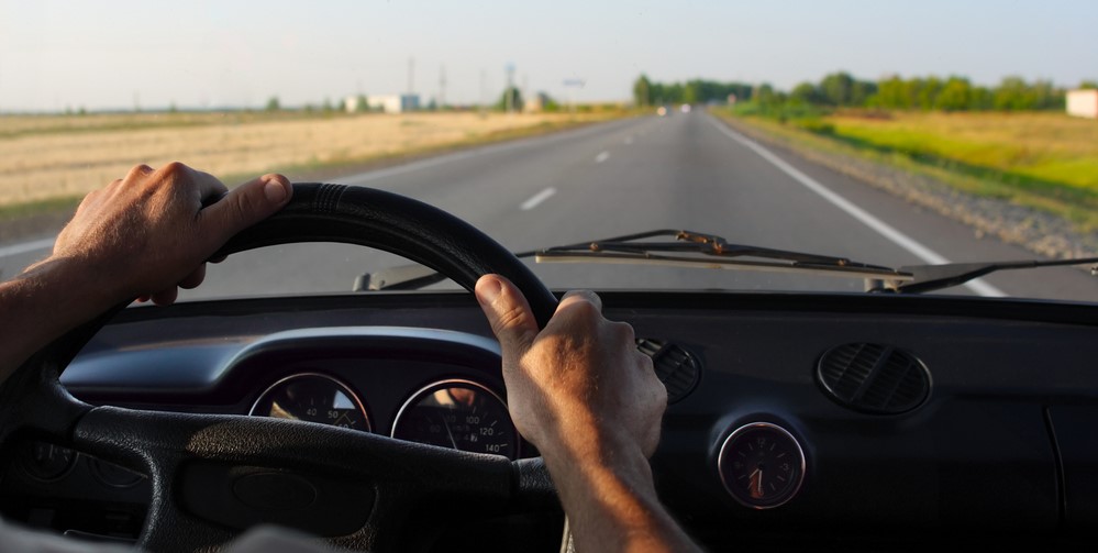 Hands on the steering wheel; view of the country-side while driving down a country road
