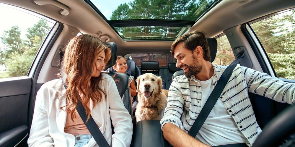 family inside of a car with their dog, parents looking back smiling at daughter and dog