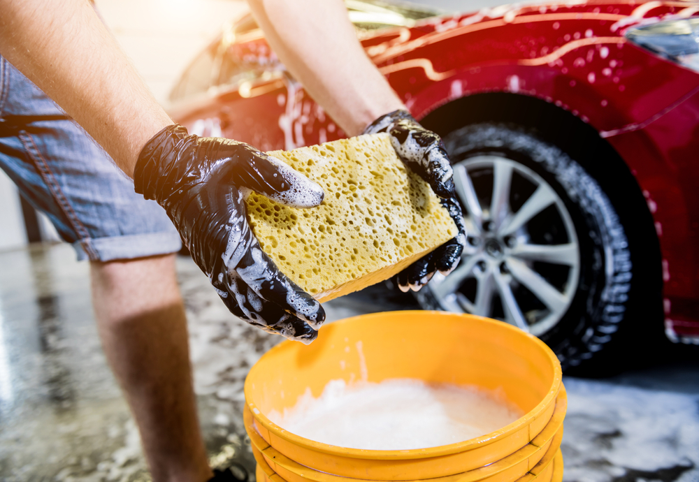 Person holding a soapy sponge while washing a red car.