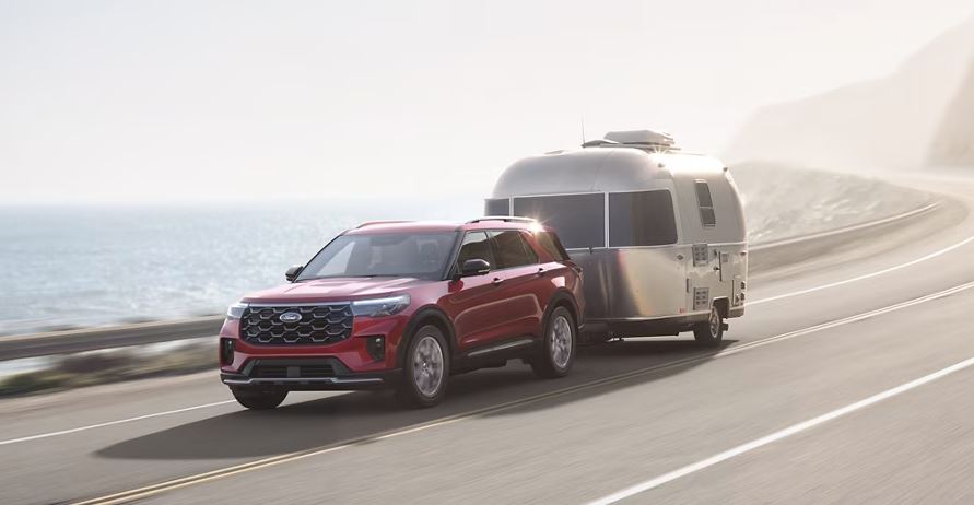 Red 2025 Ford Explorer hybrid towing a camper on a seaside highway