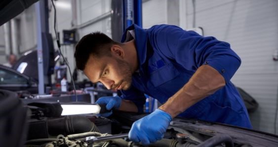 mechanic peers at vehicle's engine with flashlight