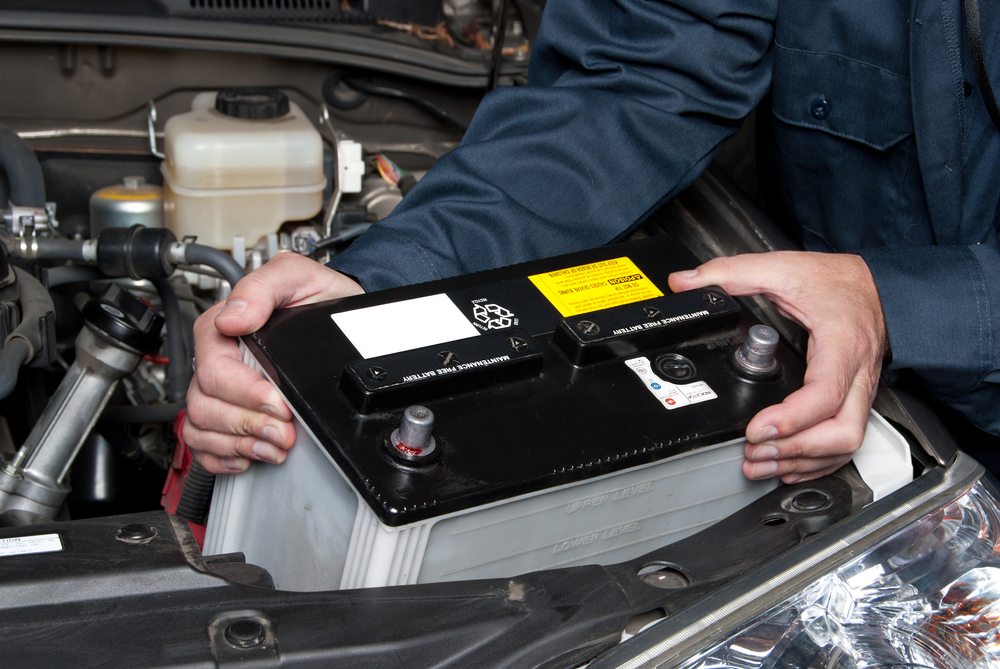 Mechanic installing a car battery under the hood.