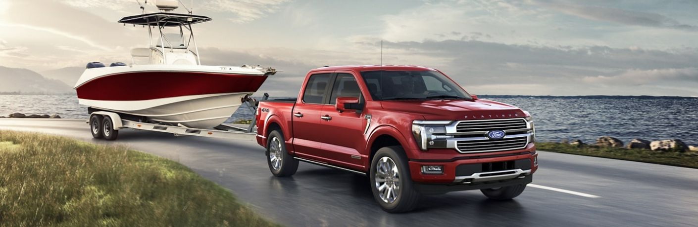 Red 2024 Ford F-150 Towing a Boat Next to Water