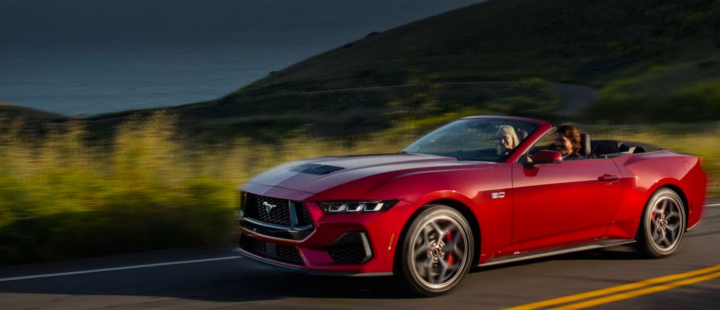 red 2023 Ford Mustang convertible driving on a shoreline road