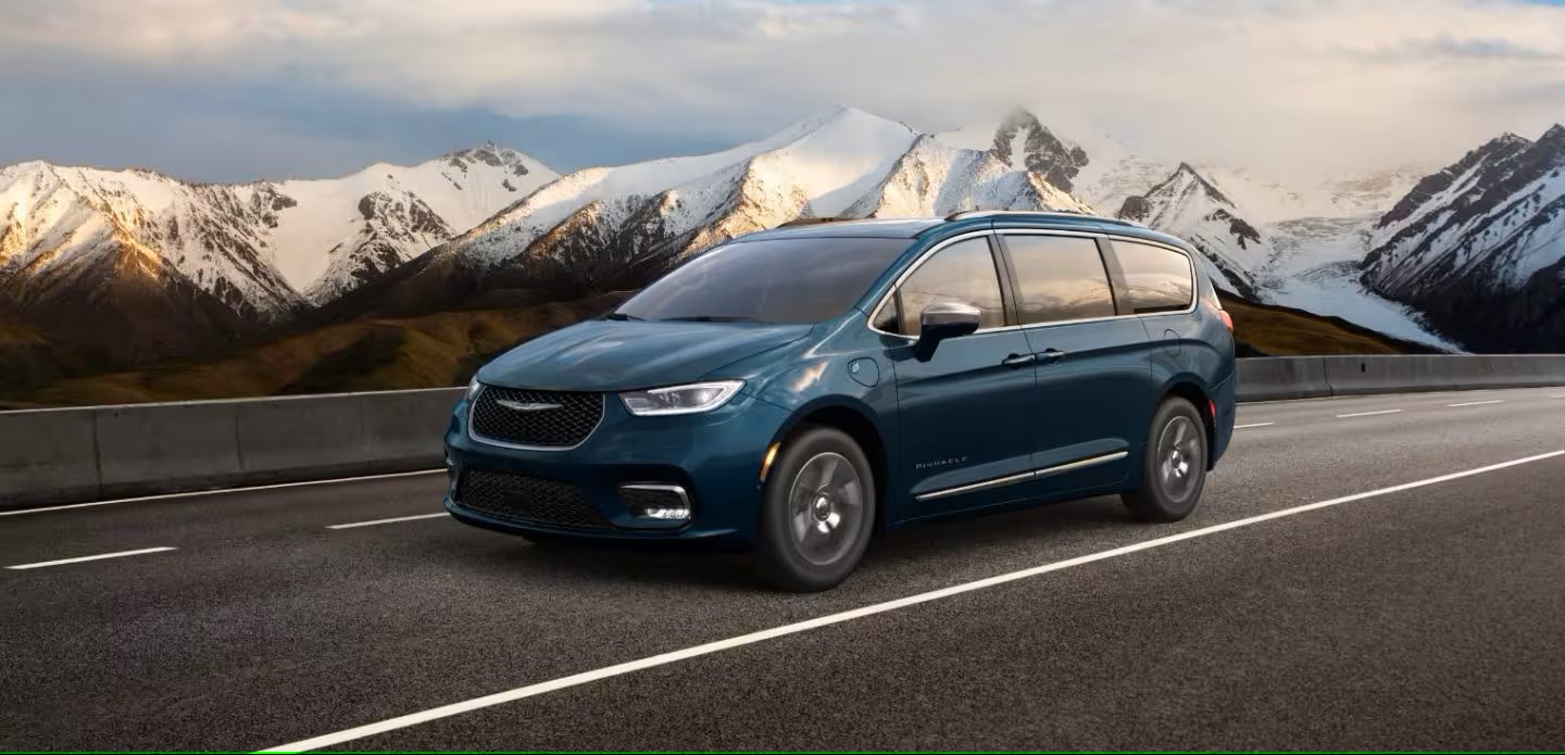 a blu minivan driving on a paved road with white cappped mountains in the background