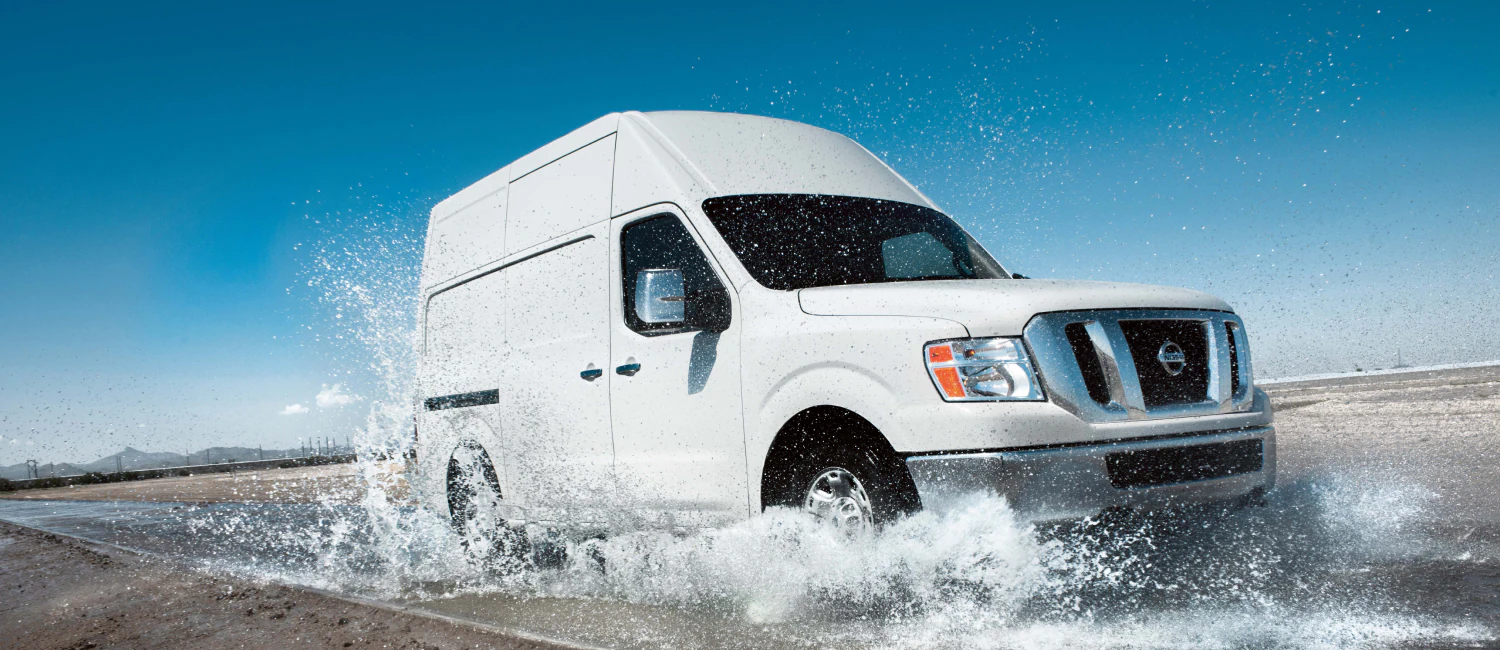 a white nissan cargo van driving through a gigantic puddle in a southwest dirt area. 