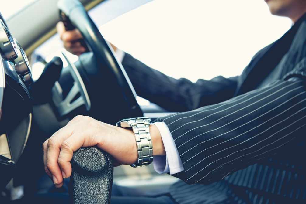 man wearing a pin striped suit and a fancy watch, driving a luxury car