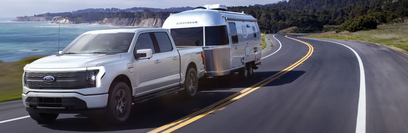 White 2024 Ford F-150 Lightning Flash Towing Trailer on Coast Road