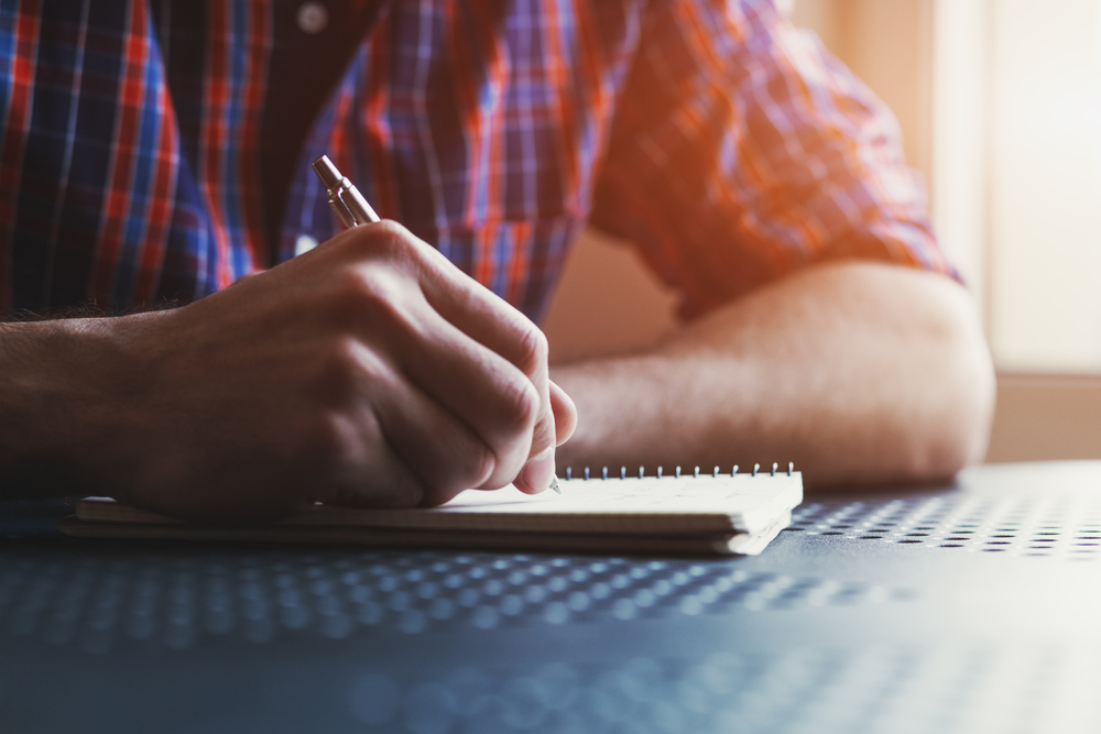 a man wearing a flannel shirt, wrting in his journal