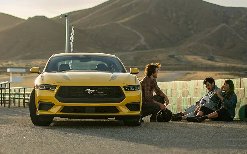 image of three people sitting beside yellow ford mustang