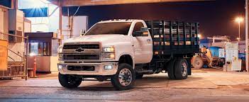 A  white Chevy Silverado 5500 commercial truck with a black bed providing routine maintenance in a commercial yard at 