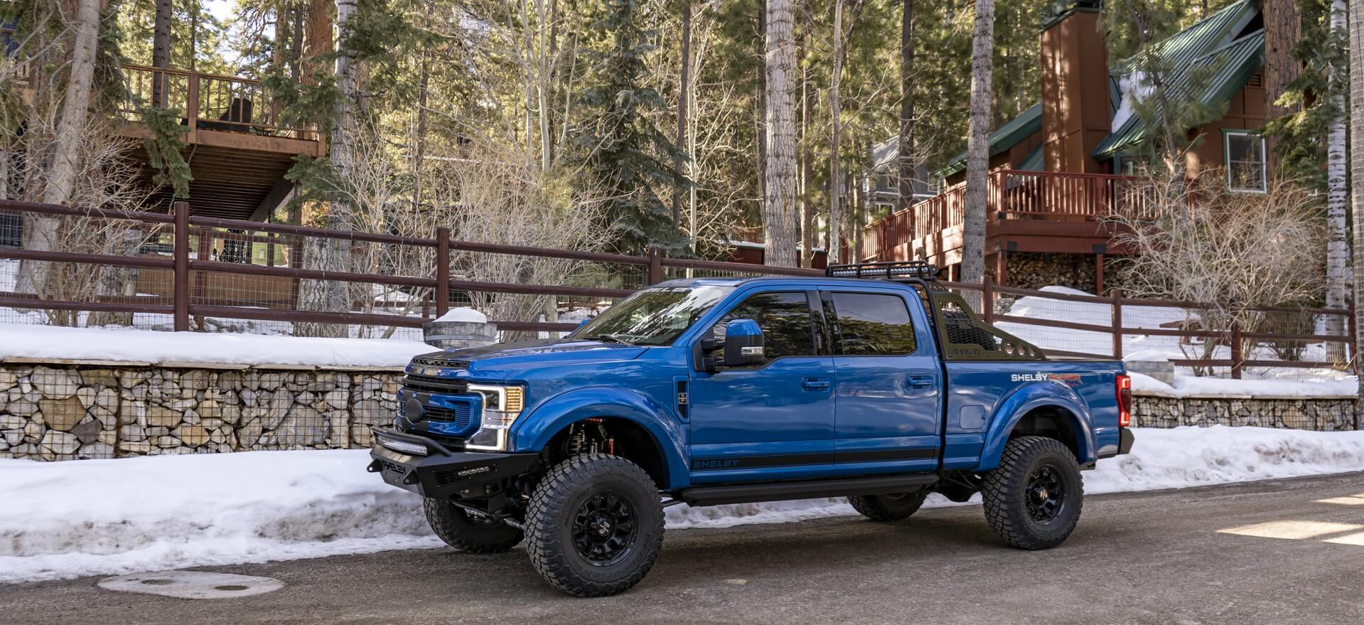 Shelby F-250 Super Baja parked by some large cabins in the woods