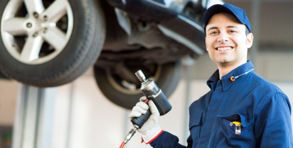 mechanic holding a tool while a tool; in background vehicle on lift