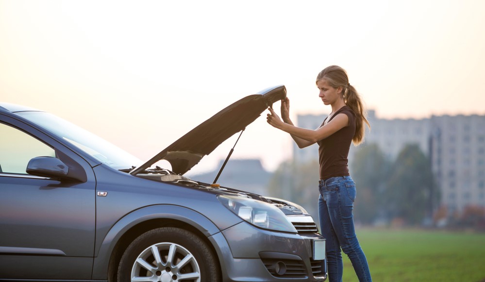 girl opens car hood on the side of the road