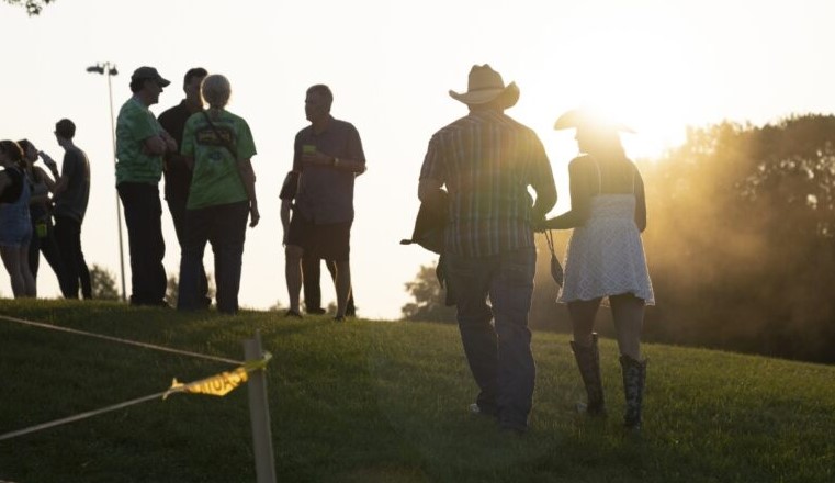 Barn Dance guests enjoying walking up a grassy hill towards other guests as the sun sets
