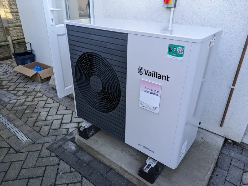 A Vaillant air source heat pump outdoor unit installed on a paved area next to a house.