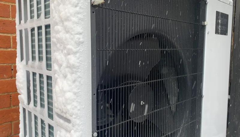 Close-up of an outdoor heat pump unit covered in frost and snow during winter.